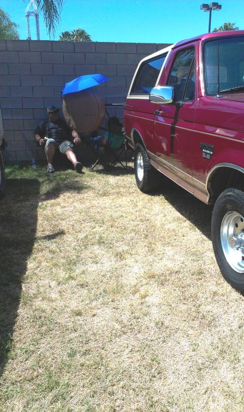 1994 Ford Bronco - A red 1994 Ford Bronco is parked outside on a sunny day, with a person relaxing in a chair nearby.