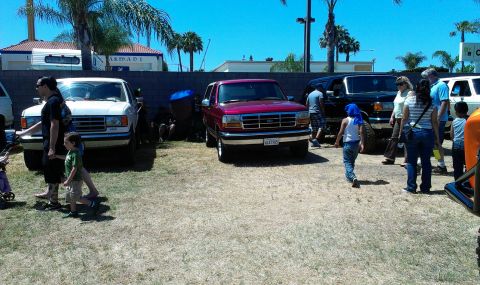 1994 Ford Bronco - A maroon Ford Bronco is parked in a lot with other vehicles and people milling about.
