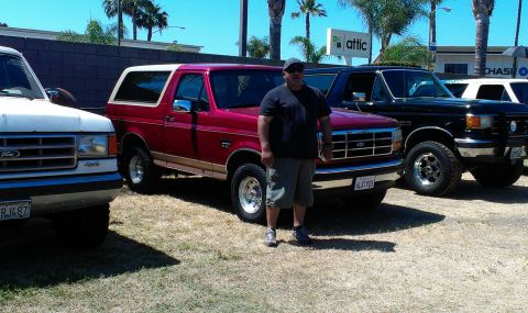 1994 Ford Bronco - Three Ford Broncos are parked outdoors on a sunny day, with a man standing between the red and black models.