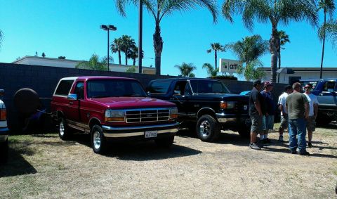1994 Ford Bronco - Two Ford Broncos, a red one and a black one, are parked outside on a sunny day.