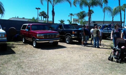 1994 Ford Bronco - Two Ford Broncos are parked outside on a sunny day, with several people gathered nearby.