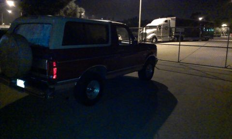 1994 Ford Bronco - A dark red Ford Bronco is parked at night, with a large semi-truck visible in the background.