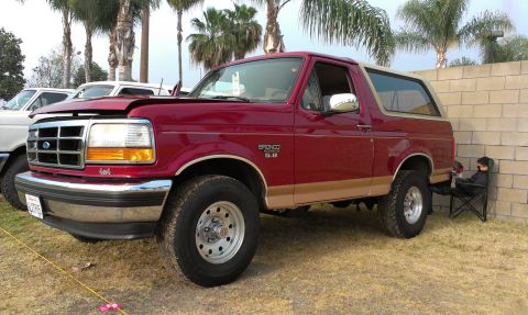 1994 Ford Bronco - A red 1994 Ford Bronco is parked outdoors with its hood open, next to a wall. Another vehicle is visible to the left.