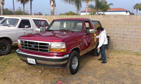 1994 Ford Bronco - A person polishes the side of a red 1994 Ford Bronco parked next to a white SUV.