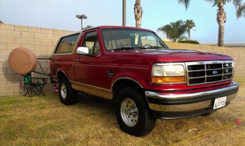 1994 Ford Bronco - This red Ford Bronco is parked on a grassy area next to a brick wall.