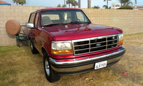 1994 Ford Bronco - This red 1994 Ford Bronco is shown from the front three-quarter angle, with a spare tire mounted on a stand to its left.