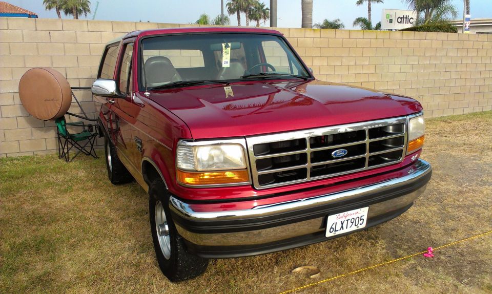 Red 1994 Ford Bronco parked on grass, front 3/4 view, chrome grille, tan spare tire cover on stand