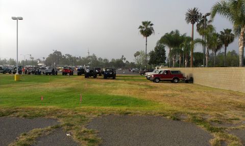 1994 Ford Bronco - A red 1994 Ford Bronco is parked beside a wall, with a gathering of other vehicles in the distance.