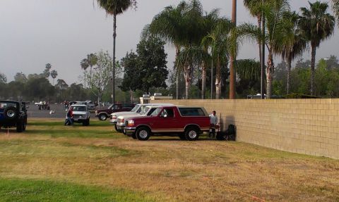 1994 Ford Bronco - A red Ford Bronco is parked next to a brick wall, with several other vehicles visible in the background.