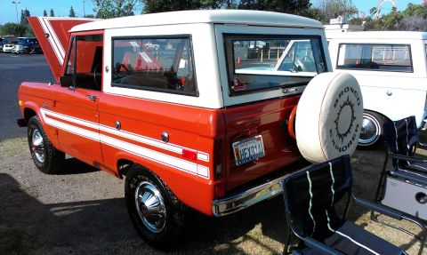 1994 Ford Bronco - This red and white Ford Bronco, with its hood open, is parked next to another Bronco. The spare tire cover reads "Bronco Explorer".