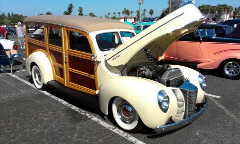 1994 Ford Bronco - A classic woodie station wagon is displayed with its hood open, revealing the engine compartment, at an outdoor car show.
