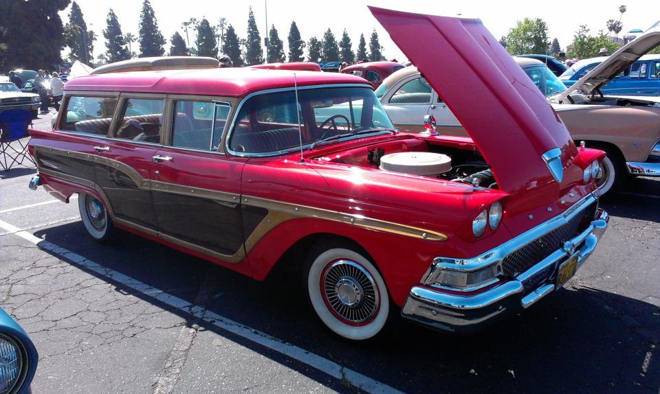 Red station wagon with wood paneling, hood open, parked at an outdoor car show. Another car is visible behind it