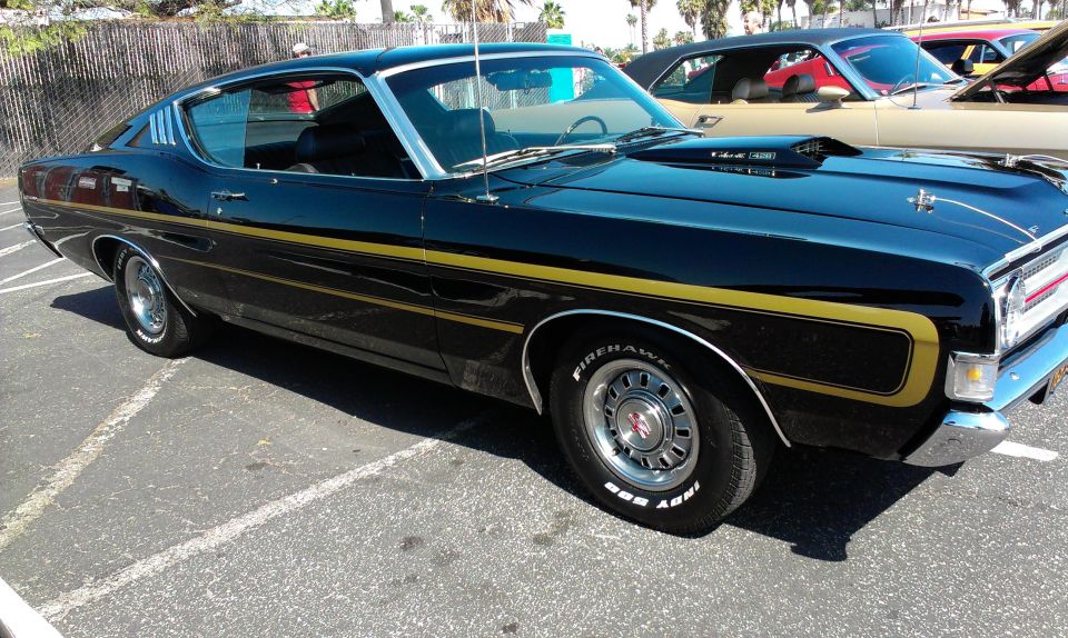 Black 1970 Ford Torino GT coupe with gold side stripes and hood scoop, parked in a lot