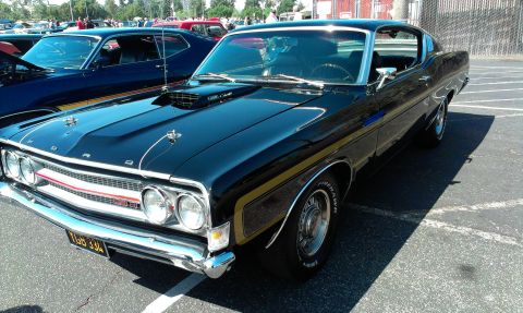 1994 Ford Bronco - A black 1970 Ford Torino GT is parked next to another classic car, a prominent hood scoop and gold racing stripes.