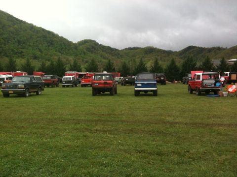 1992 Ford Bronco - A collection of SUVs and trucks are parked on a wide, grassy field under a cloudy sky.