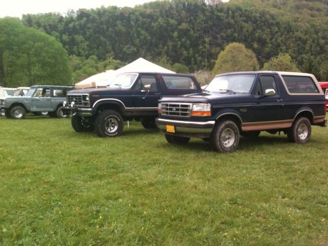 1992 Ford Bronco - A dark blue 1992 Ford Bronco with a tan top and brown trim is parked on a grassy field alongside other vehicles.