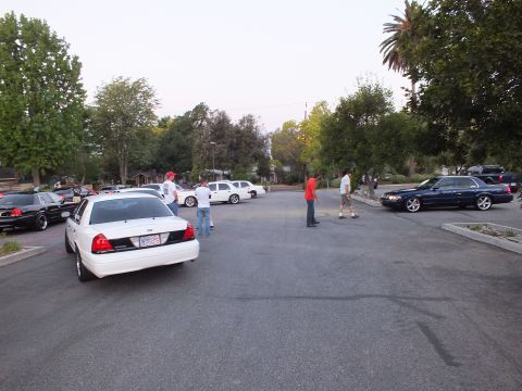 2003 Ford Crown Victoria - White full-size Ford sedan parked as attendees stand in an open lot with a dark sedan nearby