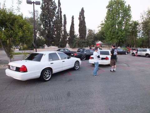 2003 Ford Crown Victoria - Profile of a white full-size Ford sedan in a lot as attendees stand around other parked cars