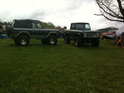 1992 Ford Bronco - Two Ford Broncos, one a pickup and the other a soft-top SUV, are parked side-by-side on a grassy field.