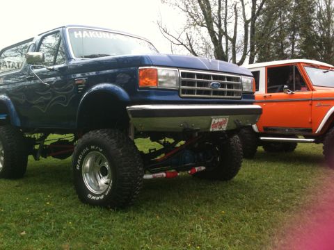 1992 Ford Bronco - A lifted blue 1992 Ford Bronco with flame decals is parked next to a lifted orange Bronco.