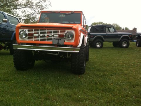 1992 Ford Bronco - Two Ford Broncos are parked on a grassy field under an overcast sky.