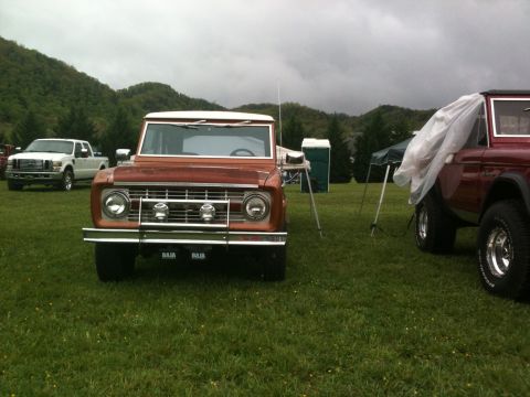 1992 Ford Bronco - Two Ford Broncos and a Ford pickup truck are parked on a grassy field with hills in the background.