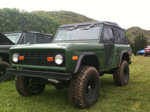 1992 Ford Bronco - This green SUV features a removable soft top and aggressive off-road tires, parked on a grassy field.