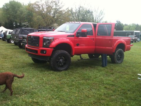 1992 Ford Bronco - A red pickup truck is parked on a grassy field with its doors open, alongside other vehicles.