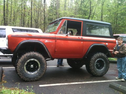 1992 Ford Bronco - This orange Ford Bronco features a lifted suspension and oversized tires, with a young boy standing nearby.