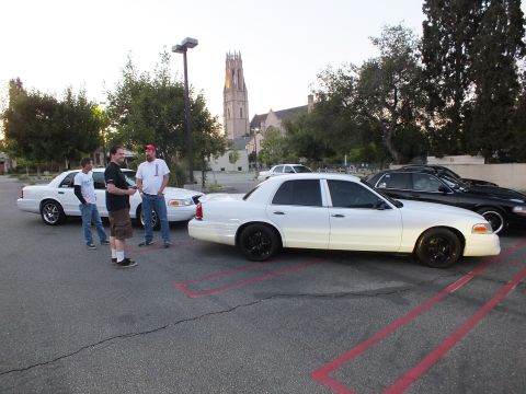 2003 Ford Crown Victoria - Lowered white Ford Crown Victoria on black rims sits in a red-striped parking lot by a church