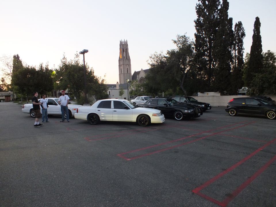 Row of Ford Crown Victoria sedans parked in a church lot at dusk with a tower behind