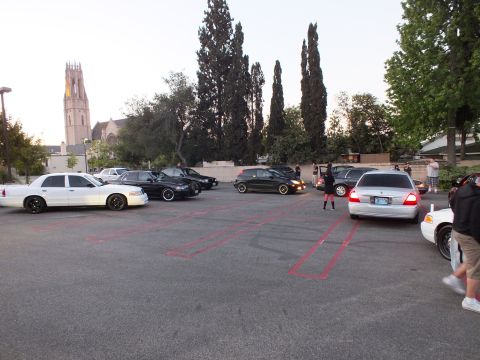 2003 Ford Crown Victoria - Wide view of a parking-lot car meet with sedans and people near a lit church bell tower