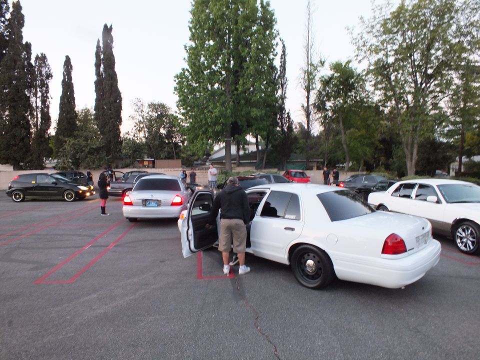 White Ford Crown Victoria with door open as a man stands beside it in a lot at dusk