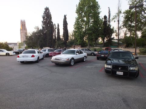 2003 Ford Crown Victoria - Crown Victoria sedans in white, silver and black parked in a lot below a church bell tower