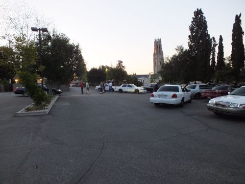 2003 Ford Crown Victoria - Open parking lot with white sedans and figures gathered near a tall lit church tower