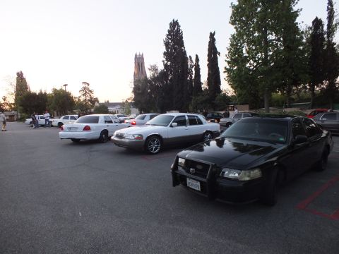 2003 Ford Crown Victoria - Black Crown Victoria with push bar parked ahead of white and silver sedans near a church