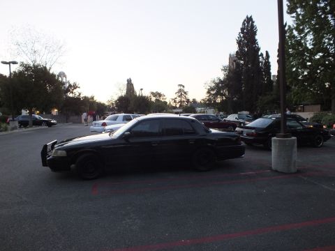 2003 Ford Crown Victoria - Side view of a blacked-out Crown Victoria with brush guard parked in a red-striped lot