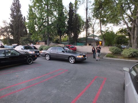 2003 Ford Crown Victoria - Gray Grand Marquis on lace-spoke wheels parked in a lot while two men stroll past