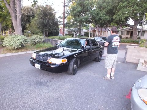 2003 Ford Crown Victoria - Man takes a photo of a black Crown Victoria parked on a tree-lined neighborhood street