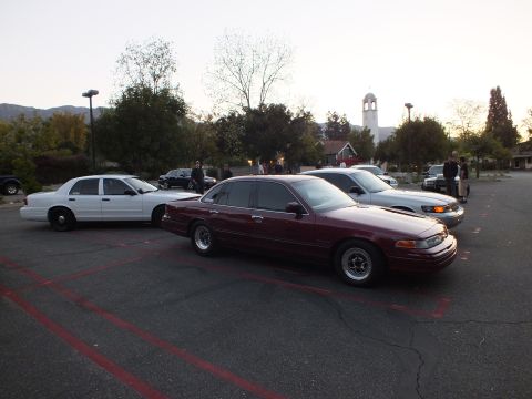 2003 Ford Crown Victoria - Maroon Crown Victoria on steel wheels parked next to a white sedan near a church tower
