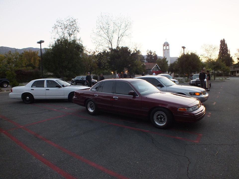 Dark red Ford Crown Victoria parked beside a white sedan in a lot at dusk
