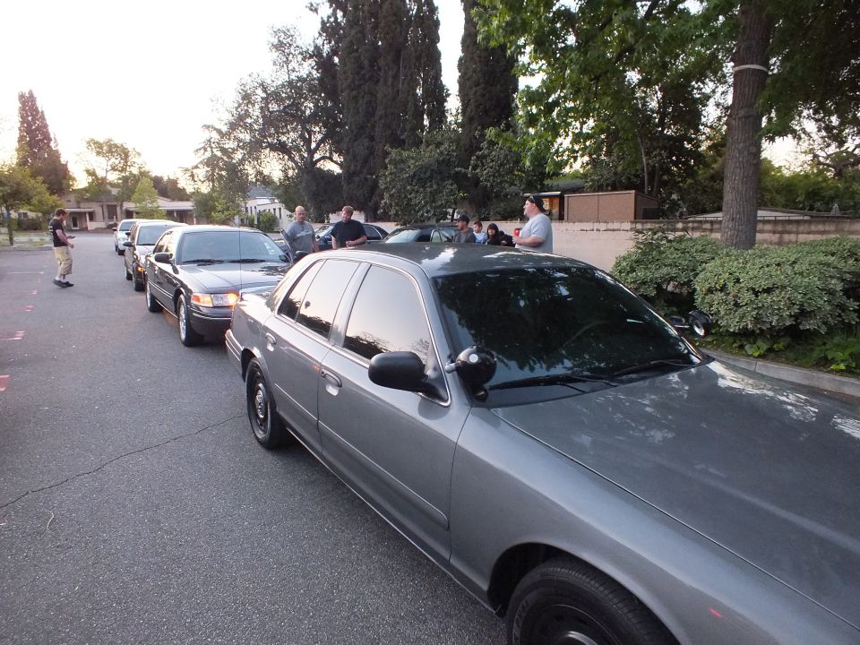 Gray Ford Crown Victoria parked on a street with other sedans and people behind