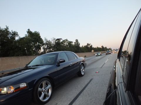 2003 Ford Crown Victoria - Dark blue Crown Victoria on five-spoke wheels cruises a freeway lane at dusk