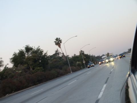 2003 Ford Crown Victoria - Oncoming and trailing cars cruise a freeway at dusk past palms, shot from a moving car