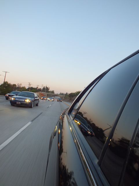 2003 Ford Crown Victoria - Glossy black sedan flank fills the frame as cars cruise a freeway lane behind at dusk