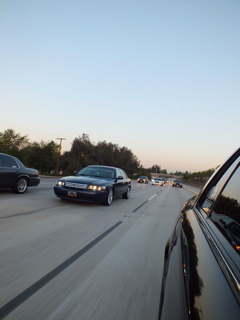 2003 Ford Crown Victoria - Dark blue Crown Victoria leads a pack of cars down a freeway lane at dusk