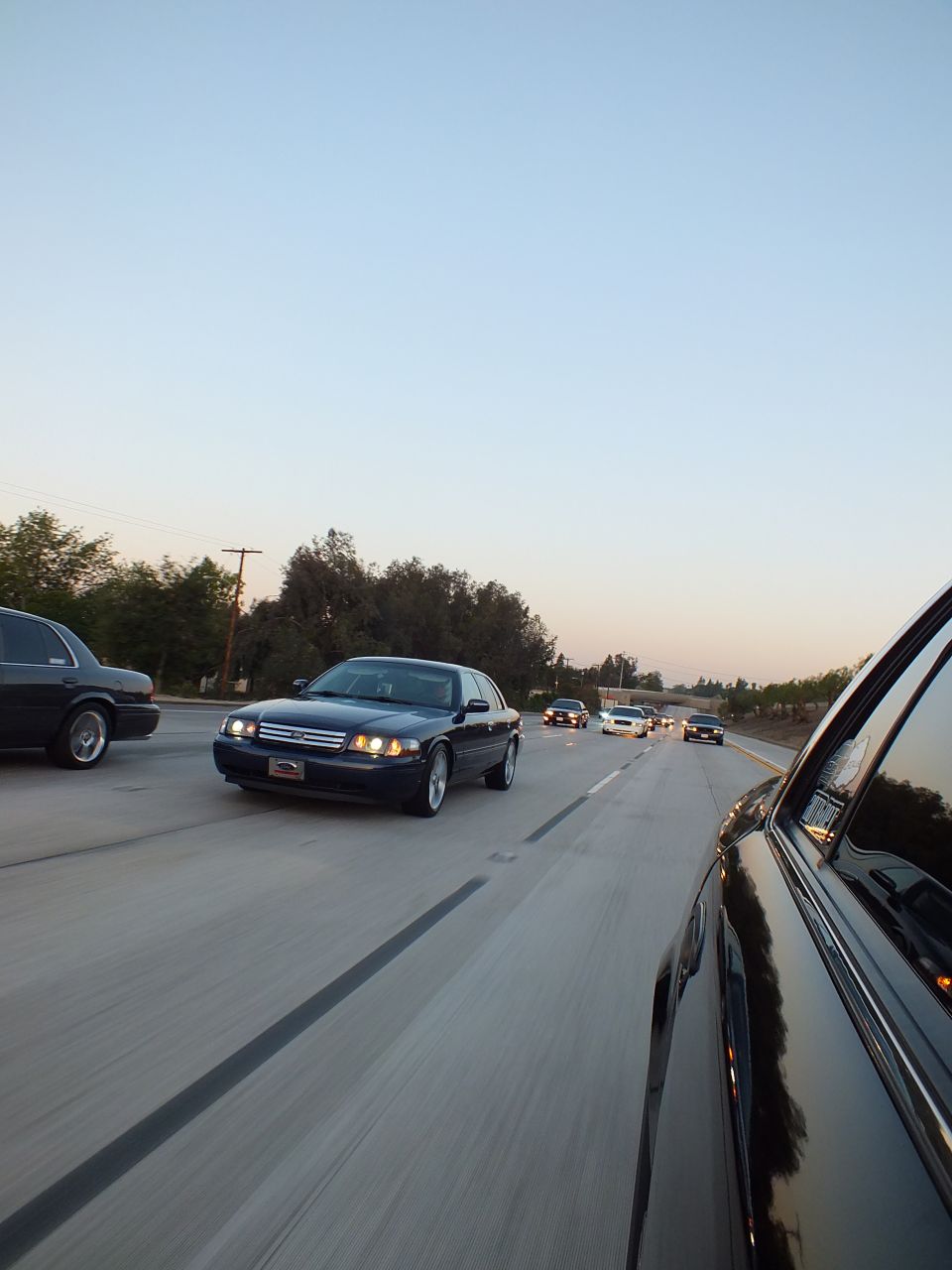 Dark blue Ford Crown Victoria with headlights on driving a freeway at dusk