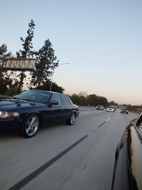2003 Ford Crown Victoria - Lowered dark blue Grand Marquis rolls under a freeway sign gantry at dusk