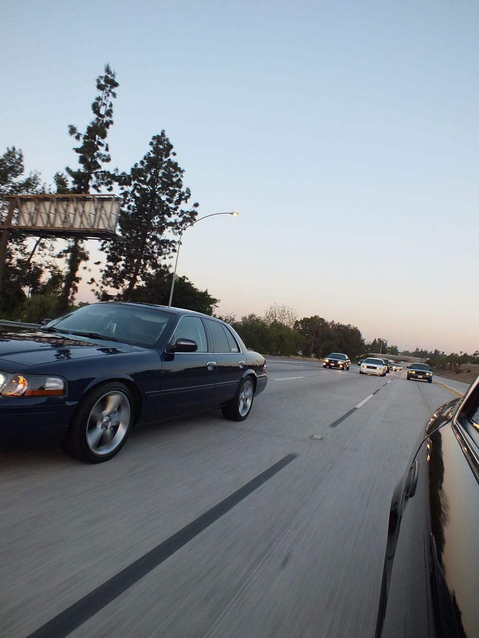 Dark blue Mercury Grand Marquis cruising a freeway past an overhead sign at dusk