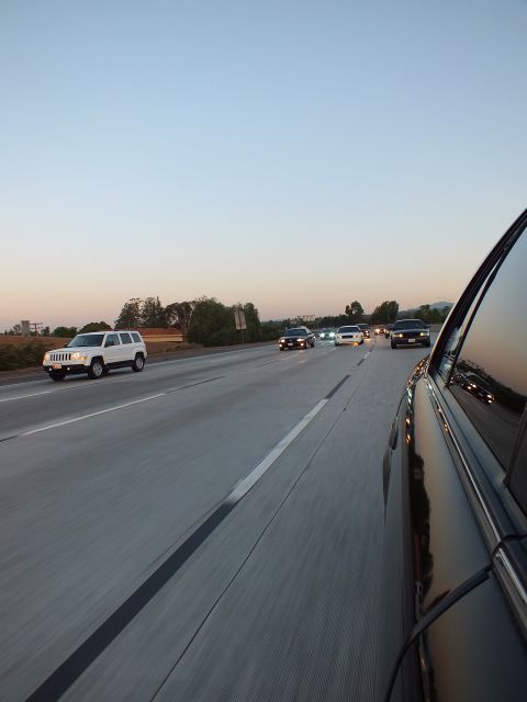 2003 Ford Crown Victoria - White compact SUV passes on a multilane freeway at twilight; mirrored car door fills the frame edge.